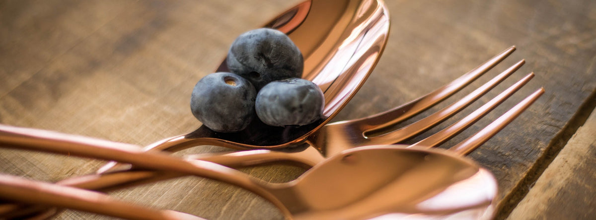 Copper Cambridge flatware with blueberries in the spoon on a wooden table