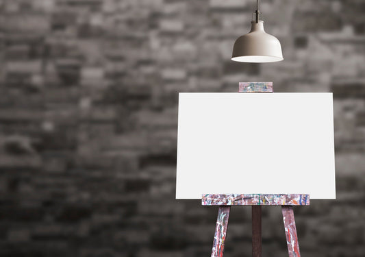 A blank canvas on a wooden easel under a single spotlight against a dark brick wall