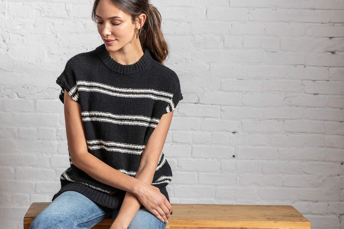 Model in a black and white striped Lilla P sweater sitting on a wooden bench